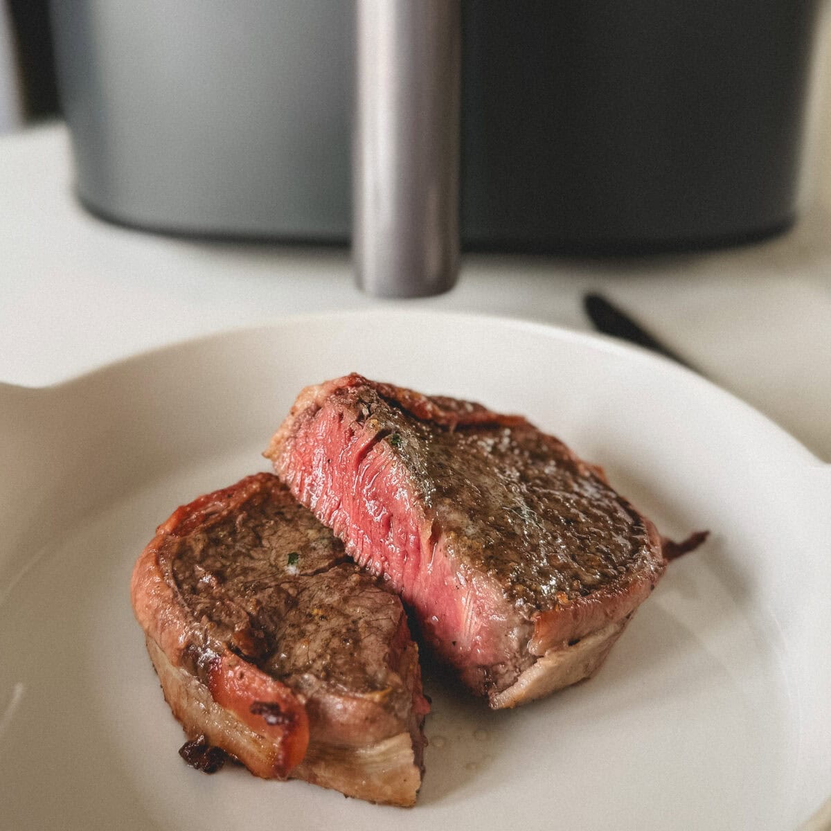tournedos coupé en deux saignant à l'intérieur dans assiette blanche devant panier d'un air fryer
