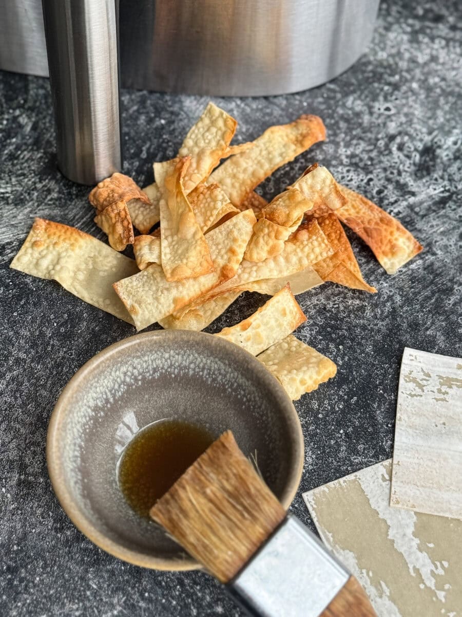 lanières de wonton frites sur comptoir bétonné avec bol d'huile et pinceau à pâtisserie