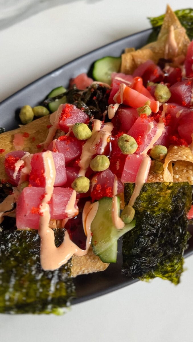 gros plan sur nachos de sushi poke, sauce épicée et dés de thon visible dans assiette oblonge noire