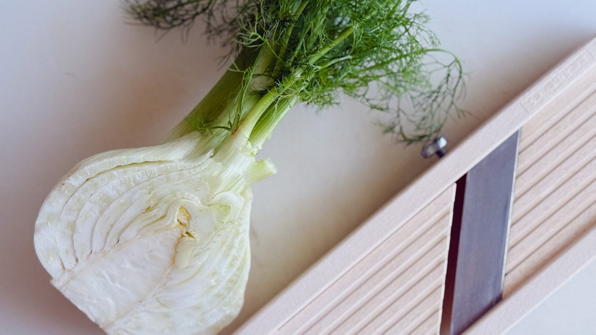 demi bulbe de fenouil avec mandoline sur planche blanche