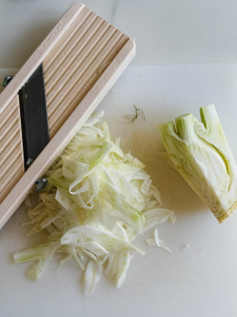 mandoline, morceau de fenouil et fines lanières de fenouil sur planche blanche