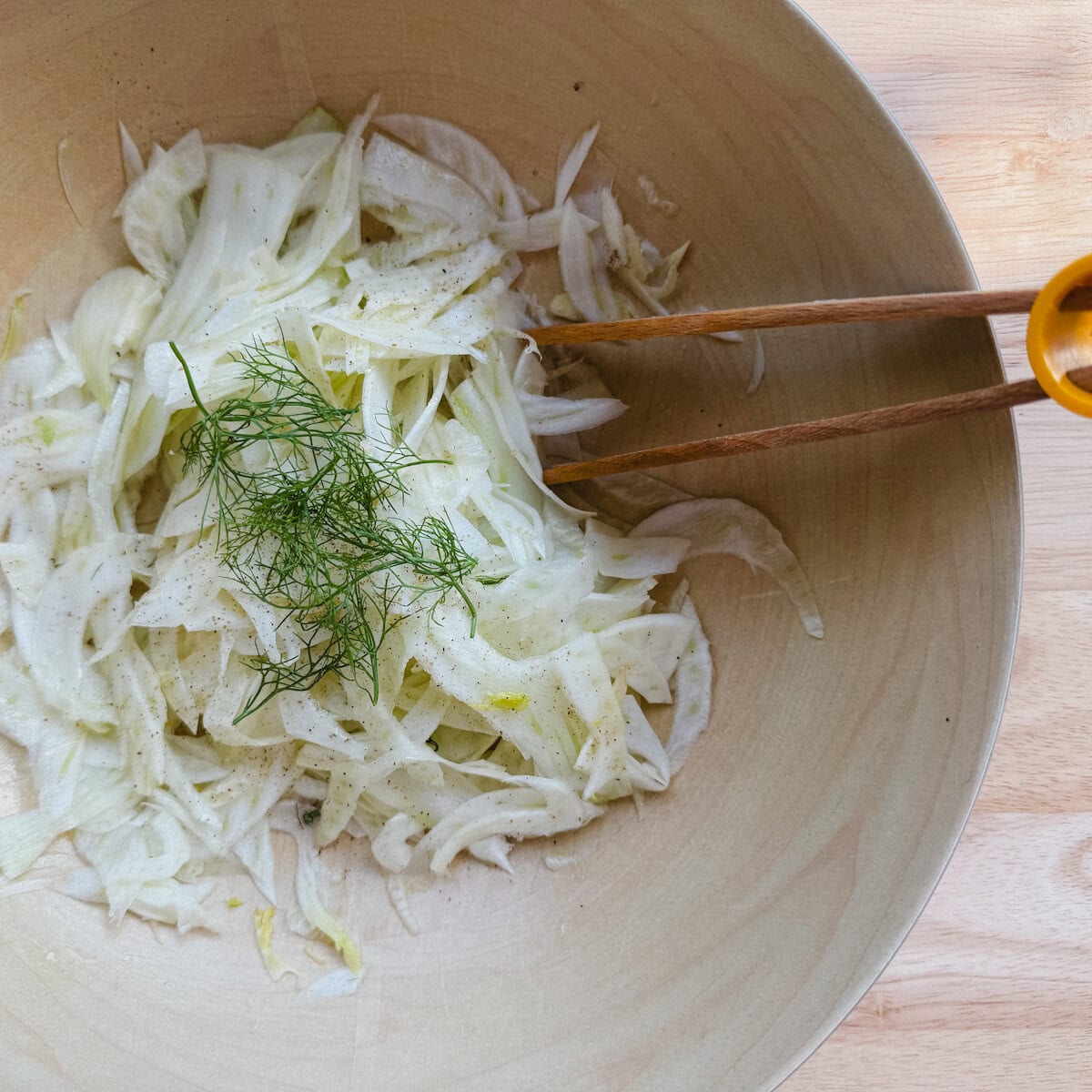 salade de fenouil dans un bol en bois avec pince de service en bois