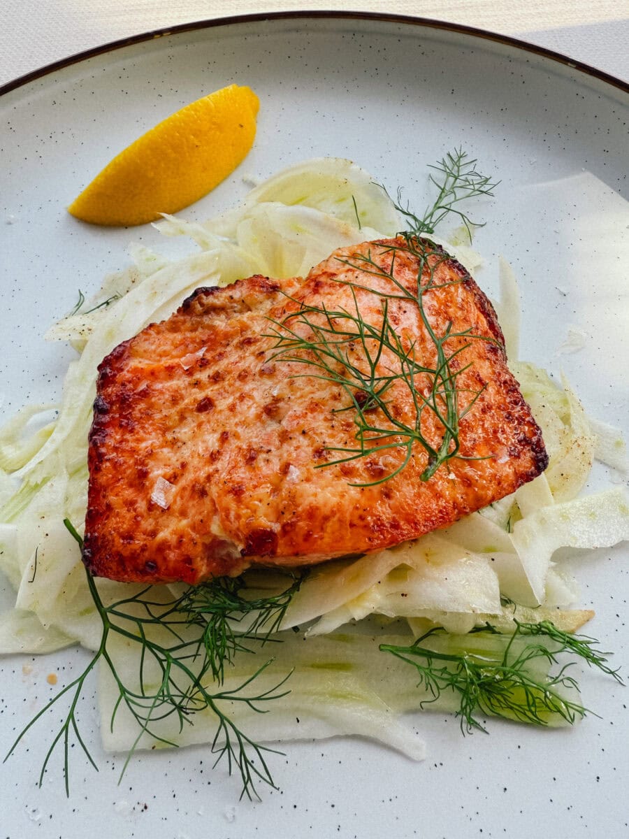 pavé de saumon grillé en sauce sur salade de fenouil dans une assiette avec quartier de citron