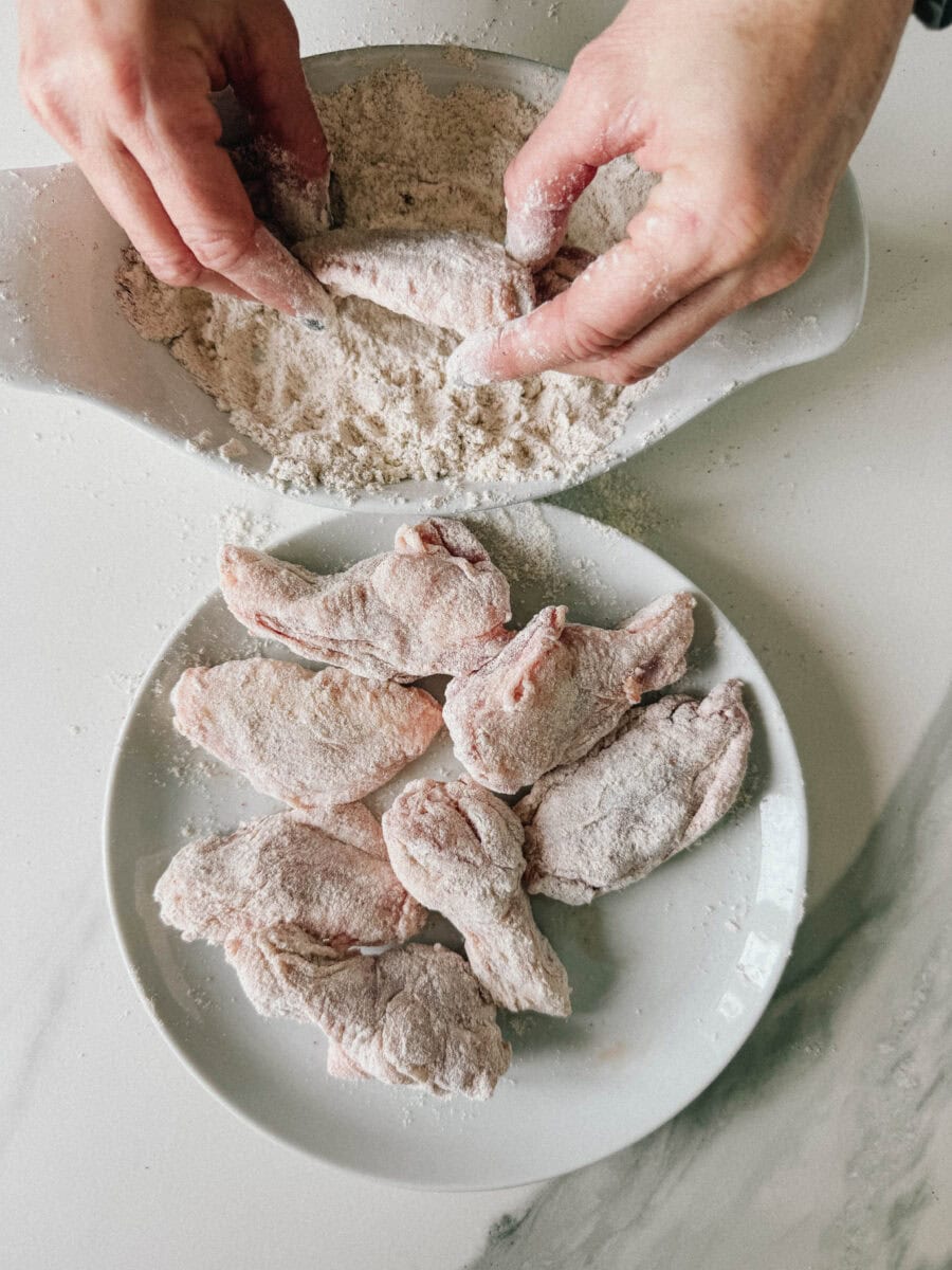 mains qui enrobent les ailes de poulet dans la farine assaisonnée