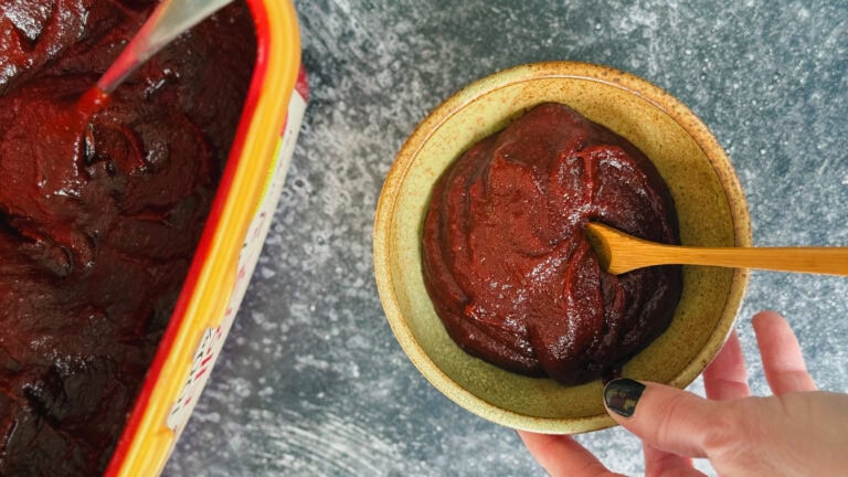 pâte gochujang dans petit bol avec cuillère en bois tenu par une main devant gros pot de gochujang