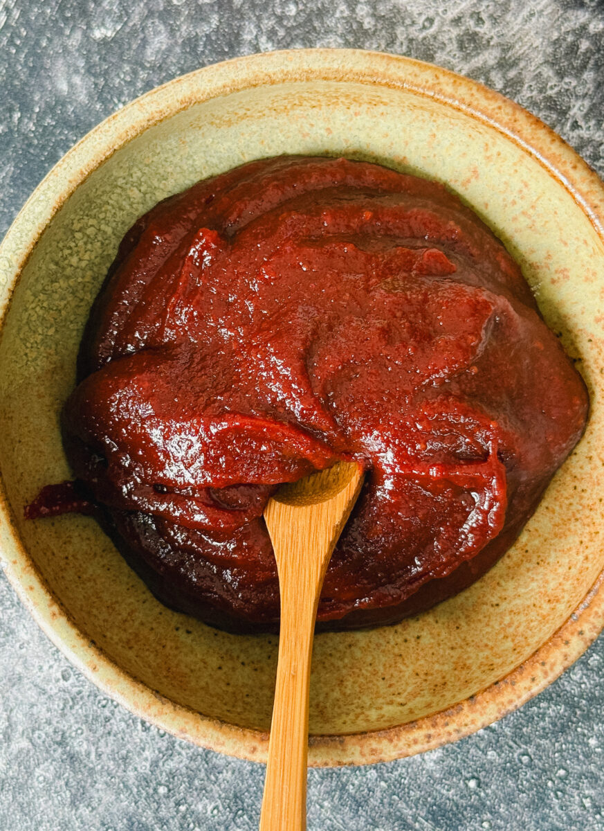 pot de gochujang avec cuillère en bois sur fond béton foncé