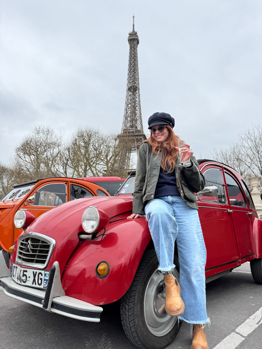 Manon Lapierre accoté sur une 2 chevaux avec la  tour eiffelen arriere plan