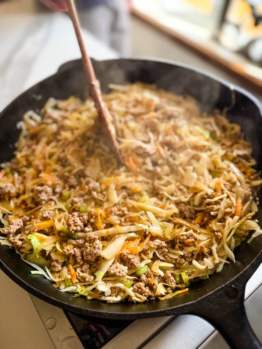 farce à egg roll qui cuit dans un poêlon en fonte avec spatule en bois qui mélange