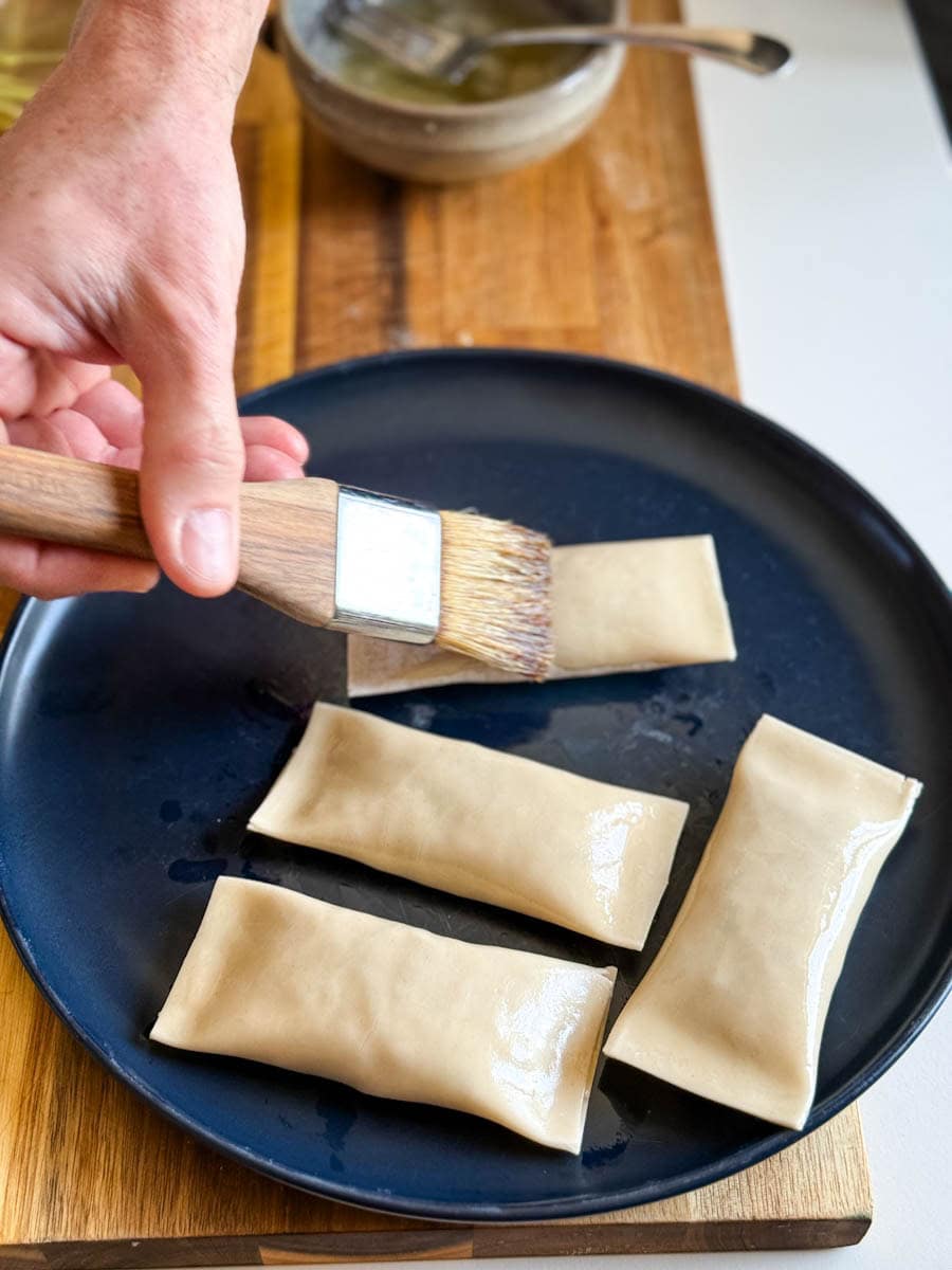 main qui badgieonne les egg rolls avec pinceau et huile