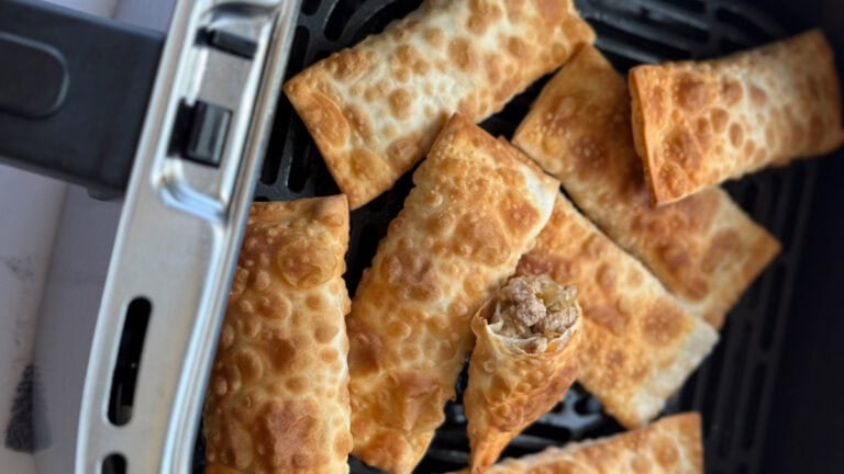 egg rolls dans le panier du air fryer, grillés avec un coupé en deux montrant la farce