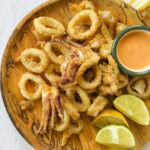 calmars frits dans une assiette en bois avec quartiers de citron vert et sauce orangée
