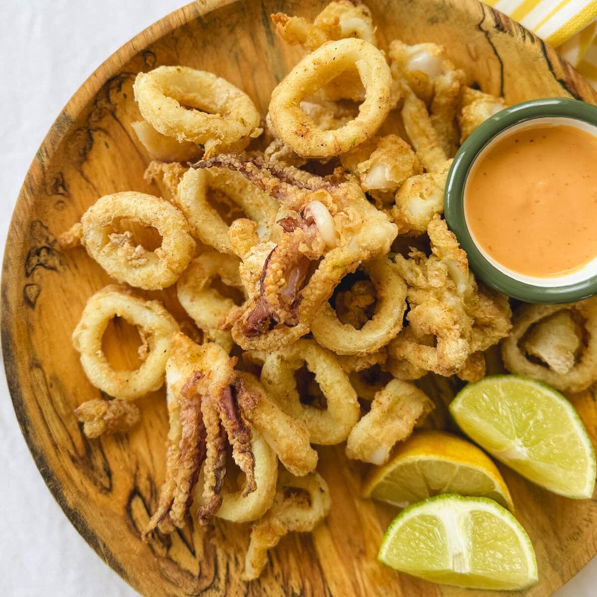 calmars frits dans une assiette en bois avec quartiers de citron vert et sauce orangée