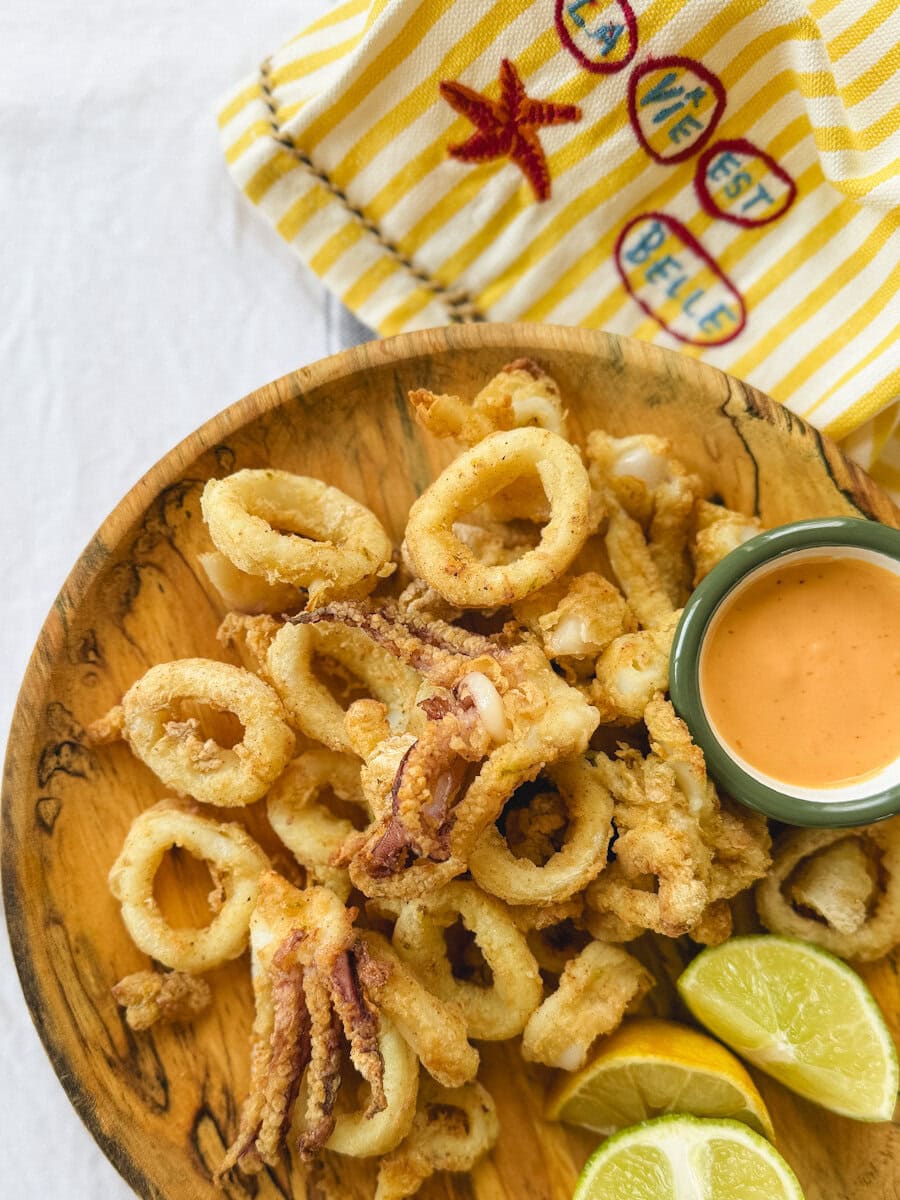 calmars frits dans une assiette en bois avec quartiers de citron et sauce rose et linge de table qui dit: La vie est belle