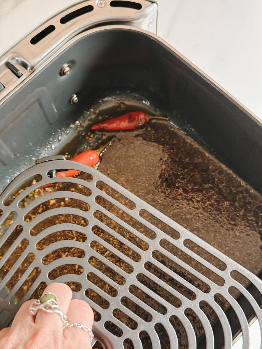 main qui dépose grille du air fryer par dessus la sauce boeuf à l'orange au fond du panier