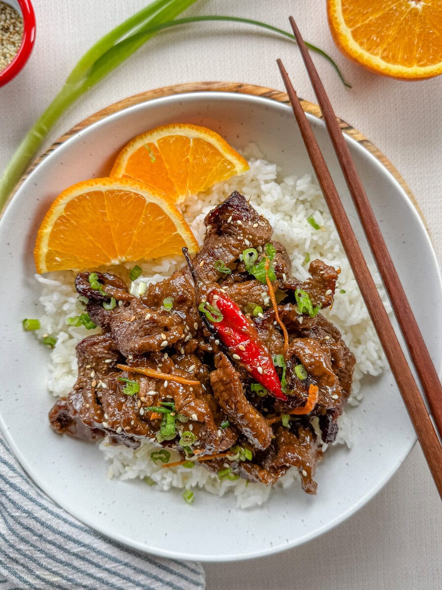boeuf à l'orange avec piment rouge sur le dessus et demies tranches d'orange sur riz blanc dans un bol blanc et chopsticks sur le dessus