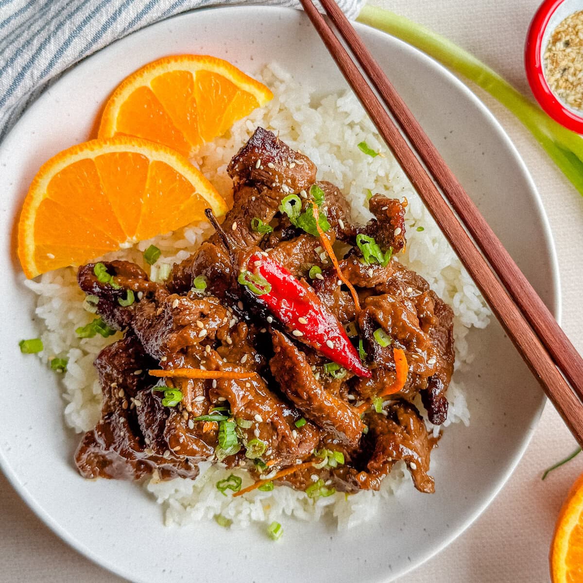 Boeuf à l'orange express sur riz dans un bol blanc avec chopsticks, tranches d'orange, piment et oignons verts