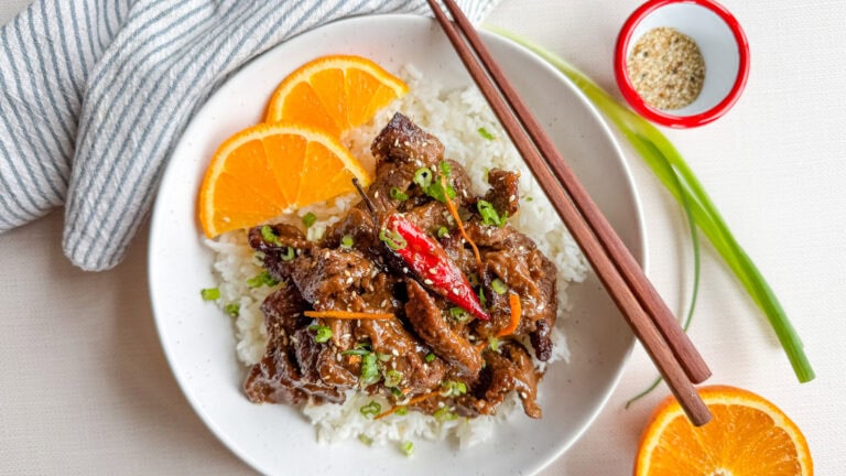boeuf à l'orange sur riz avec demies tranches d'orange, chopsticks dans un bol blanc