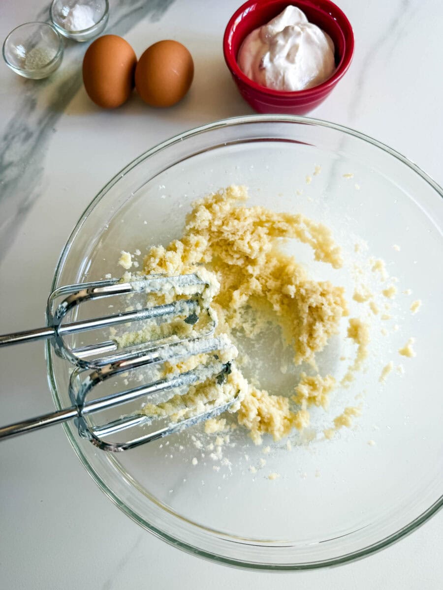 pâte à muffins aux fraises dans un bol avec fouets e mixette, 2 oeufs, bol de yogourt sur comptoir blanc marbré