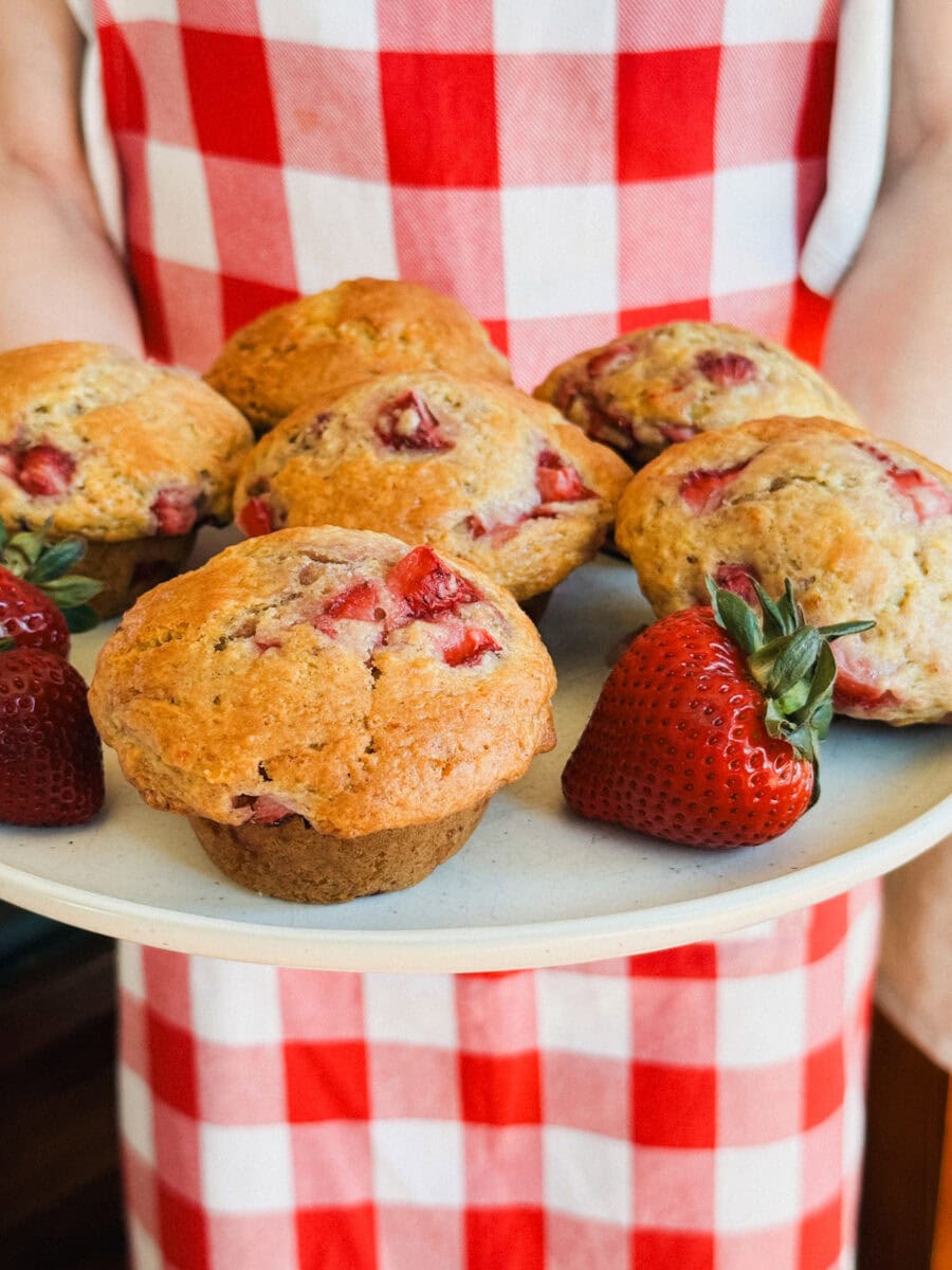 personne en tablier à carreaux rouge et blanc qui tient une assiette de muffins aux fraises