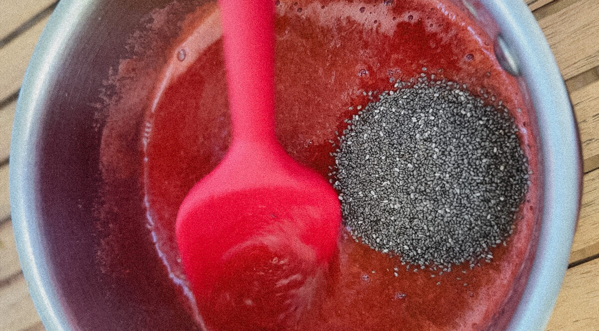 maryse rouge dans casserole de confiture lisse avec petite pile de graines de chia noires. non mélangée