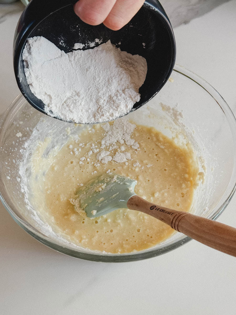 bol de farine versé par une main dans un bol de mélange à gâteau