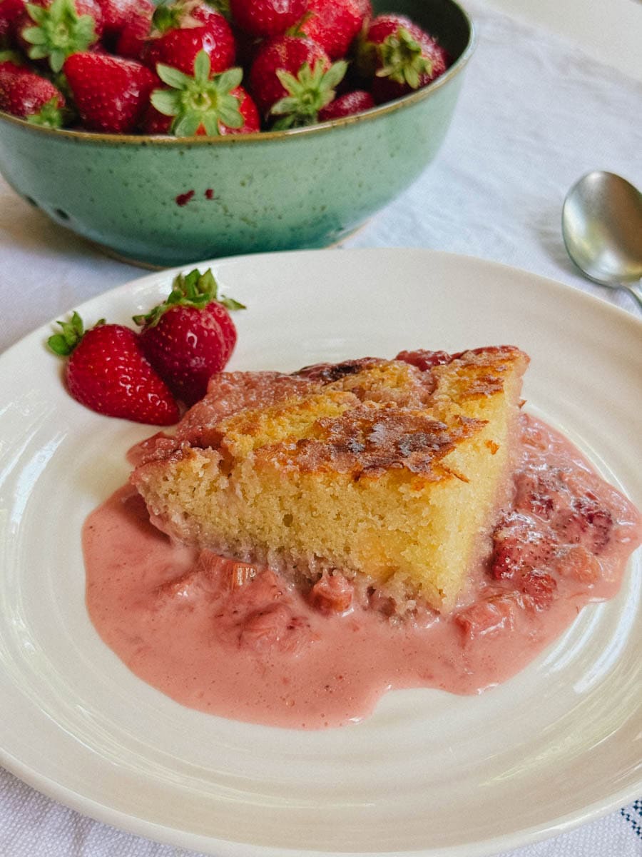 carré de gâteau blanc dans une assiette sur sauce rose crémeuse ave fraises et rhubarbe en arrière plan