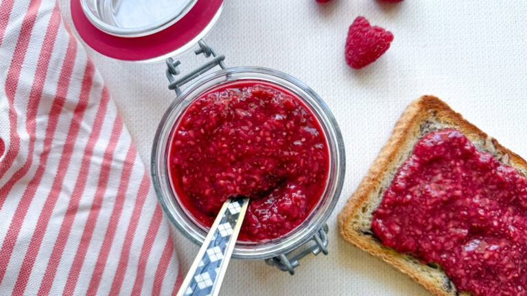 pot de confiture de framboise, linge ligné rouge et blanc, toast avec confiture sur comptoir blanc