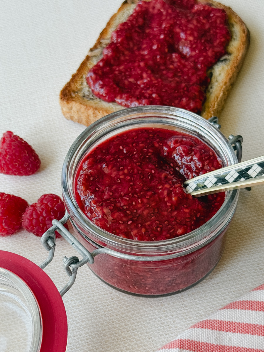 pot de confiture de framboises avec toast garnie de confiture sur comptoir blanc marbré
