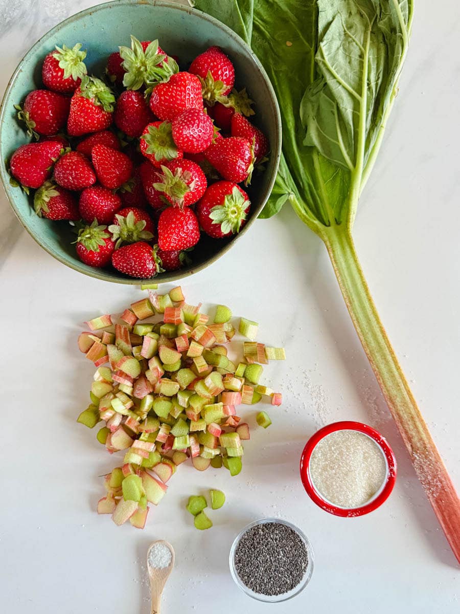 ingrédients confiture fraise rhubarbe bol de fraises, tige de rhubarbe, et rhubarbe en dés, bol de sucre et bol de graines de chia