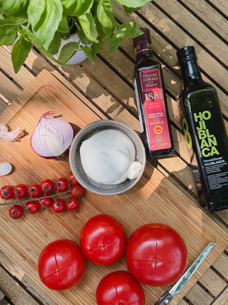 ingrédients pour soupe froide tomate burrata sur table de bois; tomates, burrata, basilic frais, bouteille d'huile d'olive et bouteille de vinaigre de xeres