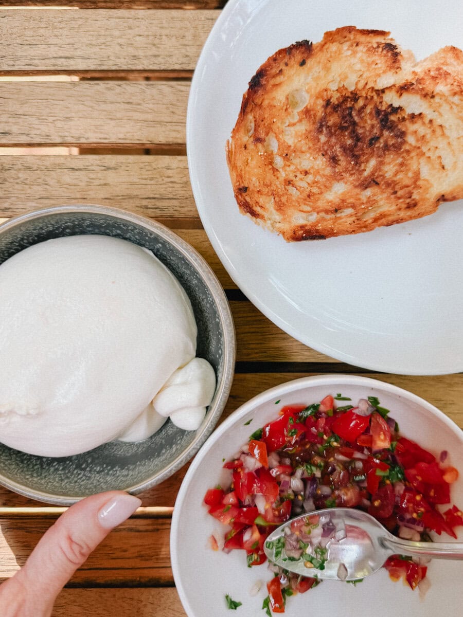 main qui tient bol de burrata, bol de salsa fraiche tomate basilic et pain rôti dans une assiette
