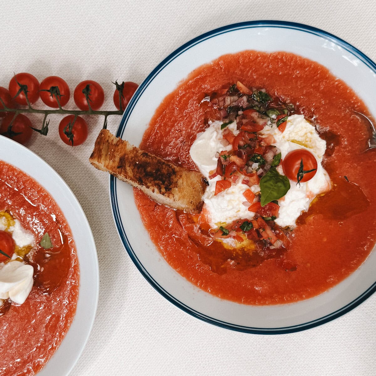 deux bols de soupe froide de tomate avec burrata, garniture de tomate fraiche, crouton de pain sur table pâte avec tomates cerises sur branche
