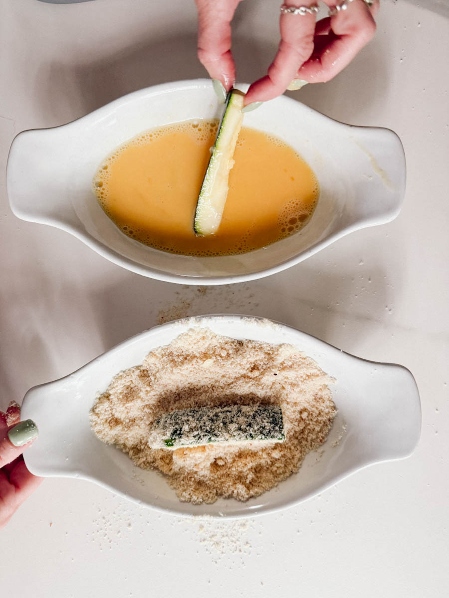 panure en 2 étapes: bol d'oeuf battu et bol de chapelure. Une main qui tient bâtonnet de courgette dans chacun des bols