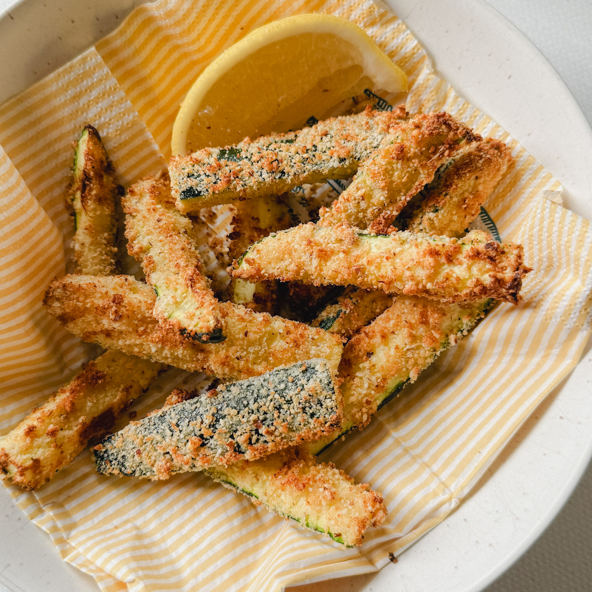 frites de courgettes panées croustillantes dansun bol sur napkin en papier lignée jaune et blanc