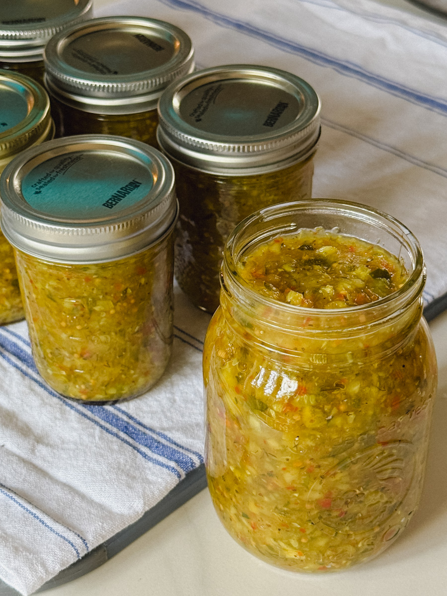 5 pots de conserve rempis de relish maison concombre courgette sur torchon de cuisie blanc ligné bleu