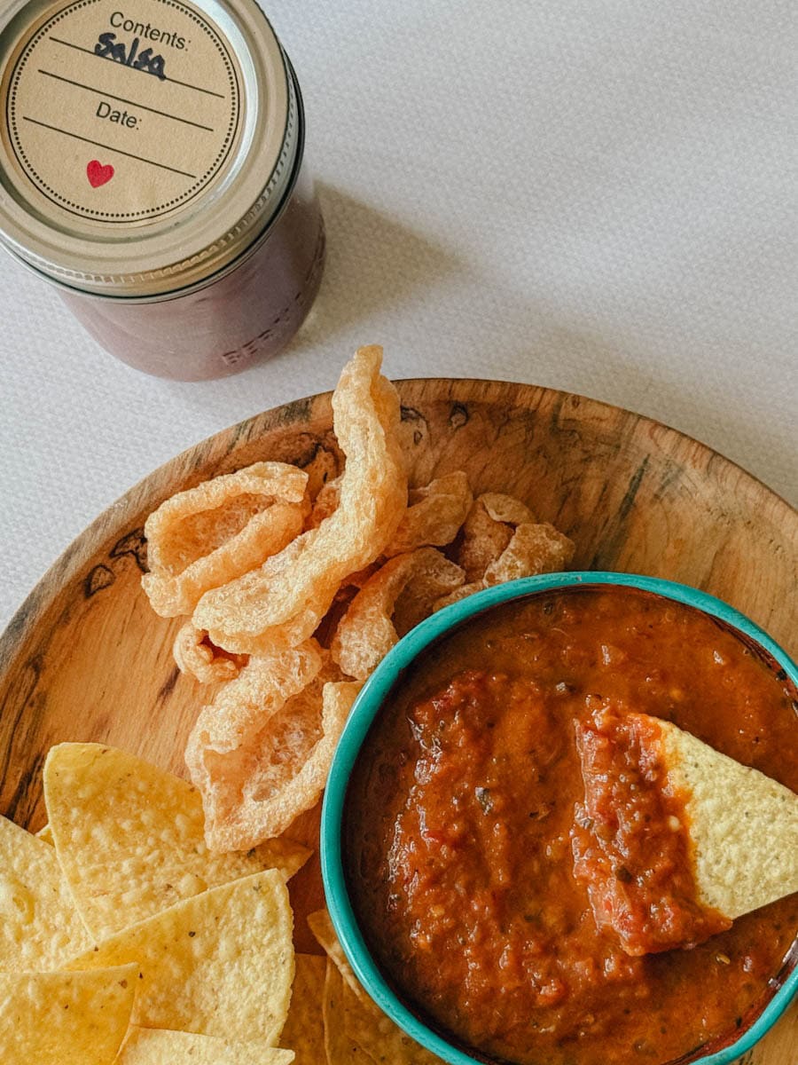 bol de salsa maison dans assiette en bois avec couennes de porc frites et chips de maïs, pot de salsa maison en conserve à côté de l'assiette