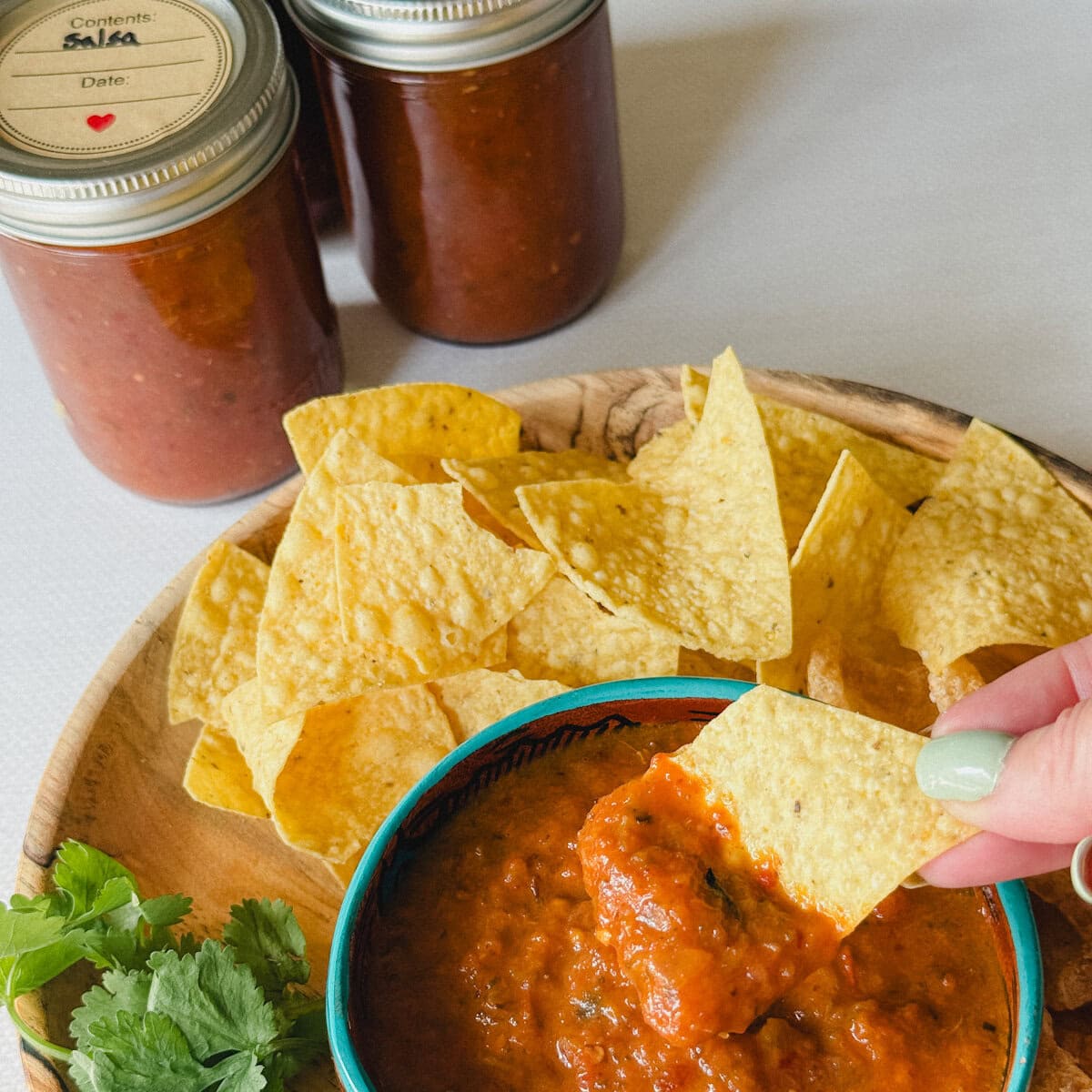 conserves de salsa maison, bol de salsa et main qui trempe une tortilla dans la salsa