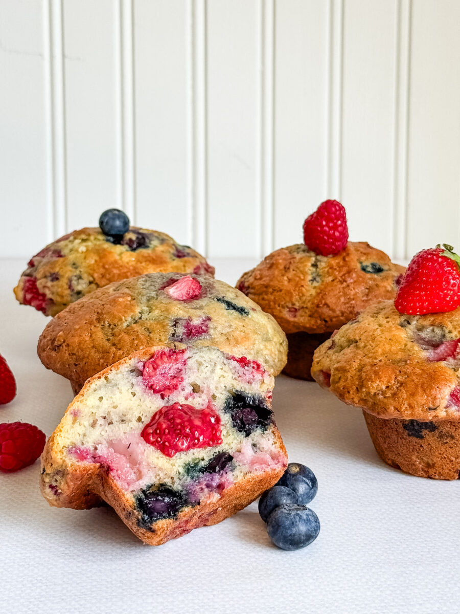5 muffins explosion de fruits sur table blanche devant mur blanc, coeur de confiture aux framboises