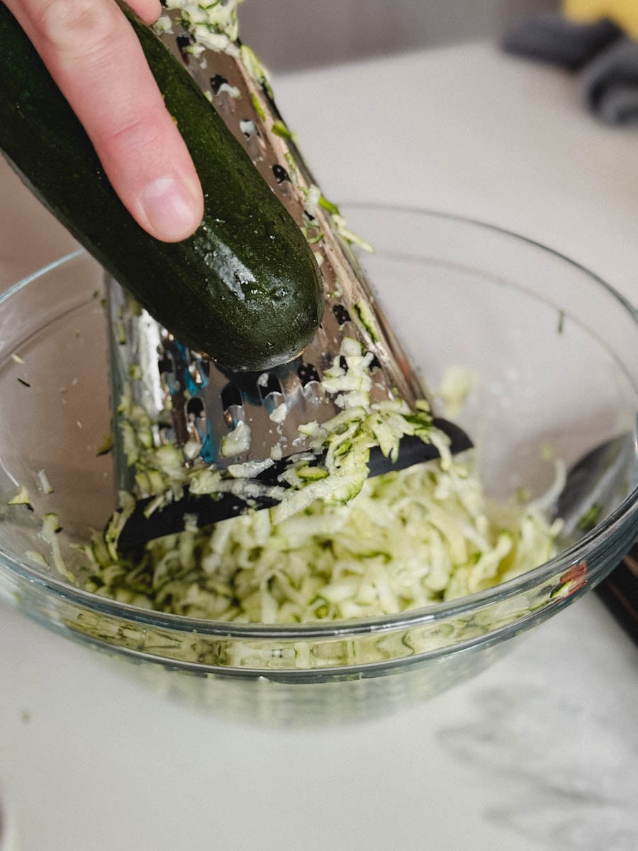 main qui râpe une courgette dans un bol 