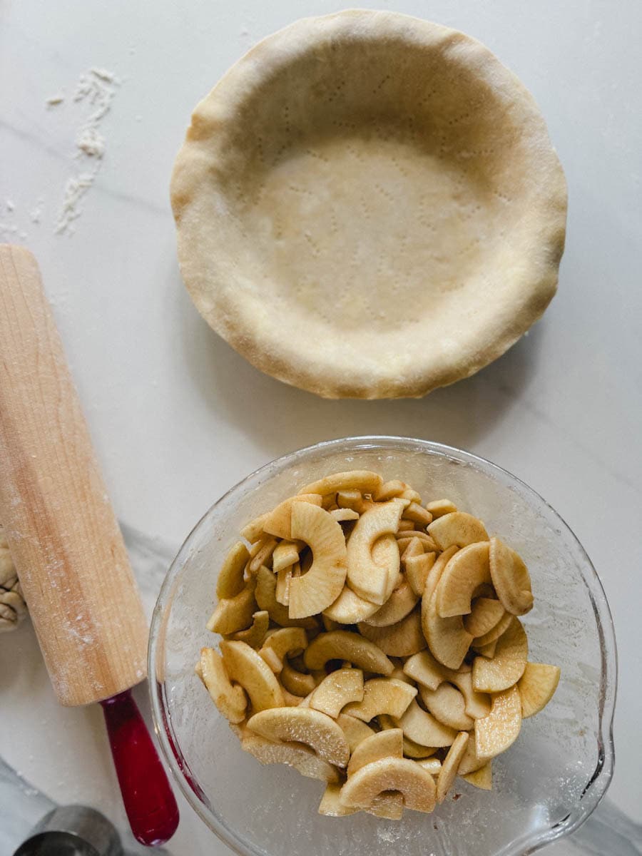 pommes et sucre dans un bol, abaisse de pâte dans le moule, rouleau à pâtisserie