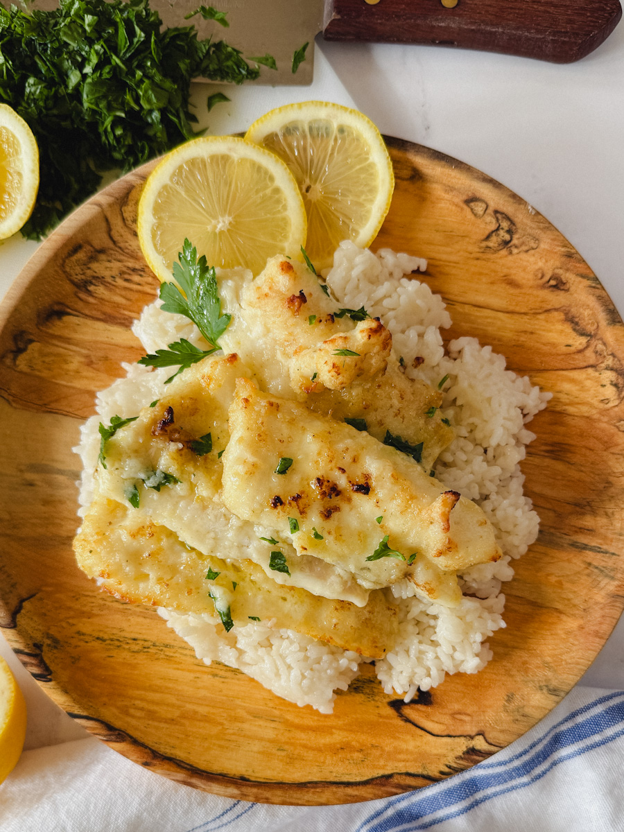 morue grillée avec sauce au citron et beurre dans une assiette en bois avec rondelles de citron et persil