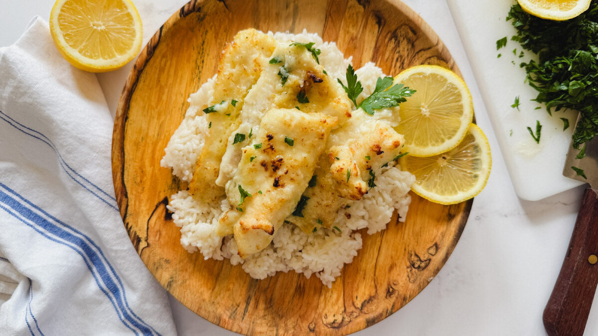 Morue en sauce beurre et citron sur du riz dans assiette en bois avec tranches de citron et persil + couteau sur le côté