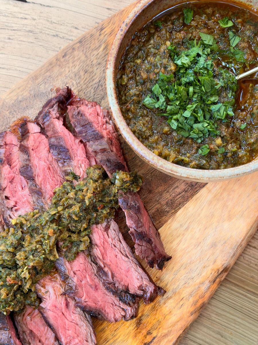 bavette garnie de chimichurri de légumes grillés avec bol de chimichurri, sur planche de bois