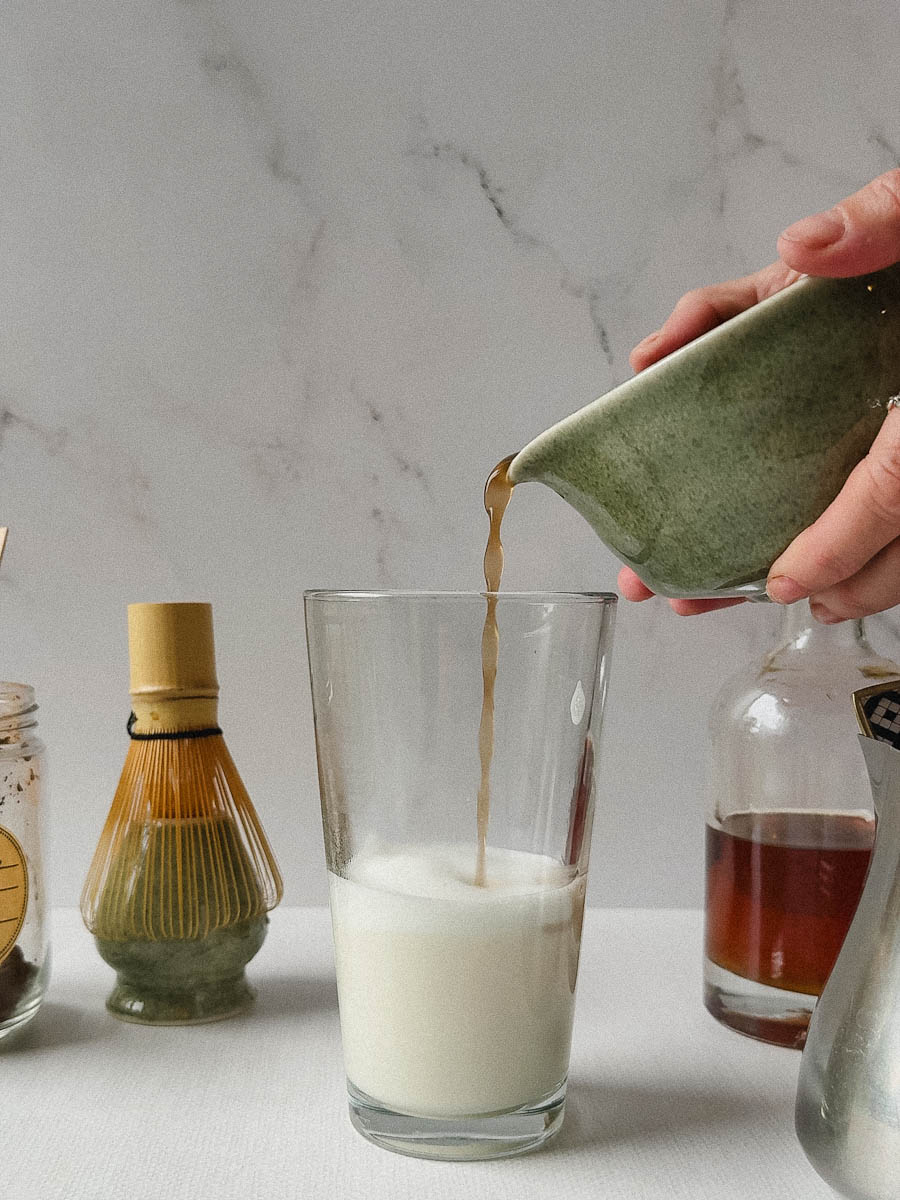 main qui tient le bol qui verse thé hojicha dans verre de  lait  
