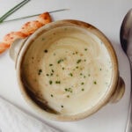 bol de crème de poireaux garni de ciboulette avec cuillère, linge, paille au fromage et tiges de ciboulette sur comptoir blanc