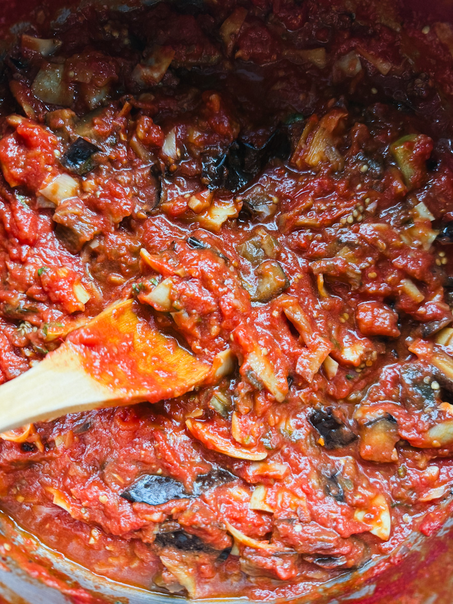 sauce pour pâtes avec aubergines et artichauts dans une casserole avec cuillère en bois