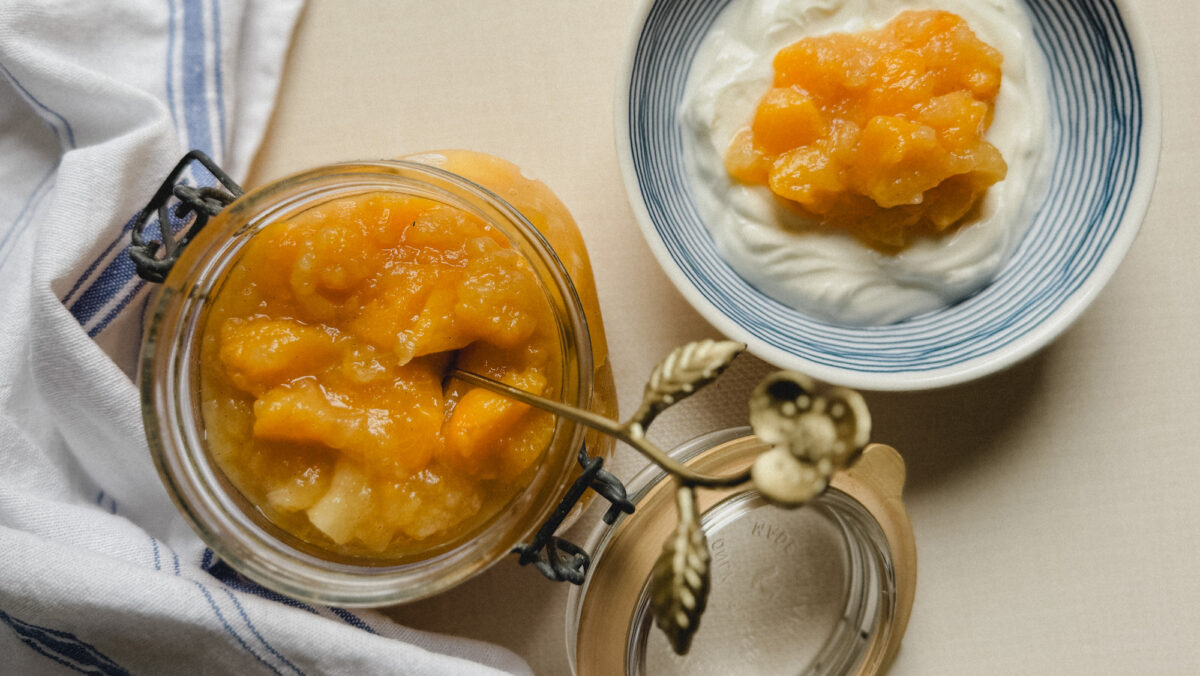 compote de pommes et pêches dans un bocal à charnière avec bol de yogourt garni de compote et torchon de lin blanc avec lignes bleues
