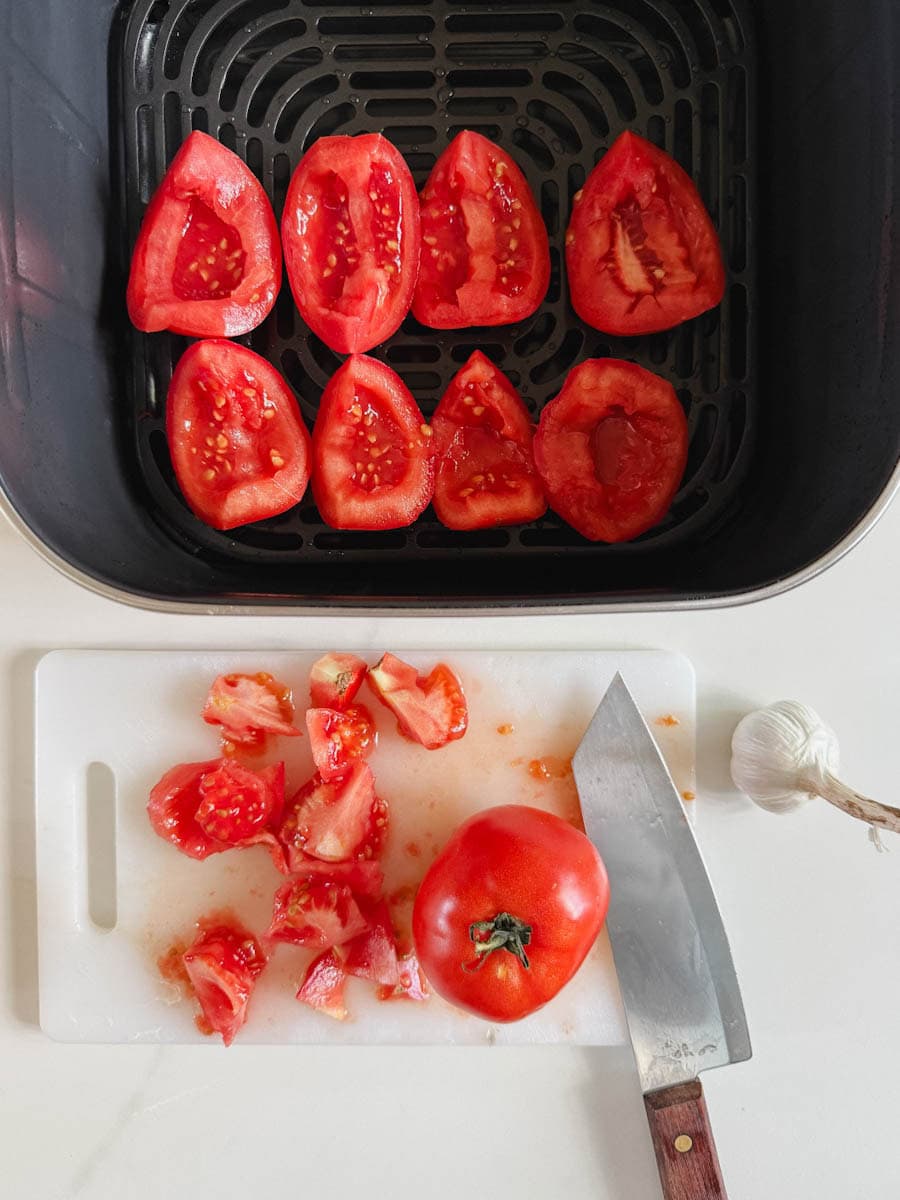 8 quartiers de tomates dans panier du air fryer, couteau avec retailes sur planche à découper