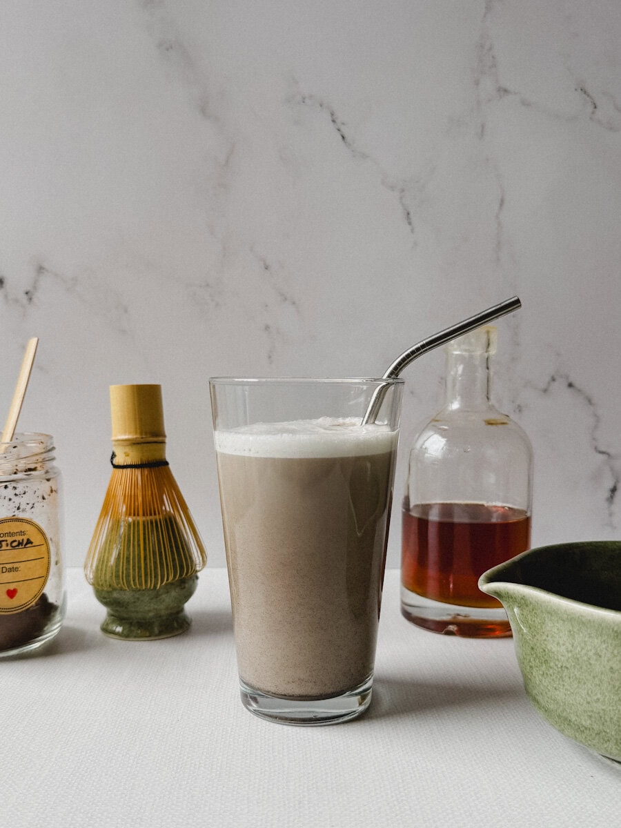 thé hojicha dans un verre avec paille en métal et instruments à matcha alentour