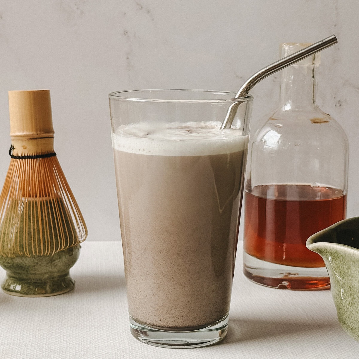 Latte au hojicha servi dans un verre avec paille en inox sur fond marbré